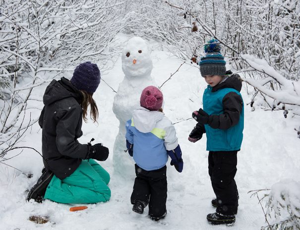 Mother with children making snowman on snowy day